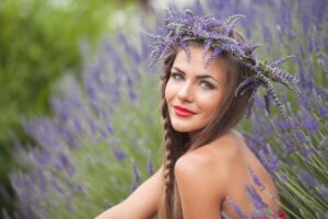 A woman with long brown hair sits amidst vibrant lavender plants, wearing a floral crown made of lavender sprigs.
