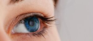 Close-up of a woman's eye with striking blue iris and long eyelashes against a soft, neutral background.