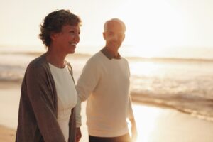 A couple strolls hand-in-hand along a sunlit beach, waves gently lapping at the shore in the background.