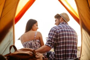 A couple sits close together inside a tent, facing a scenic view of the sunset over the water, creating a cozy atmosphere.