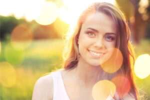A person with long, wavy hair stands in a sunlit field, surrounded by blurred golden bokeh, evoking a warm, dreamy atmosphere.
