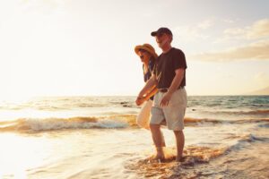 A couple strolls hand-in-hand along the shoreline, waves gently lapping at their feet, with a warm sunset casting a golden glow.