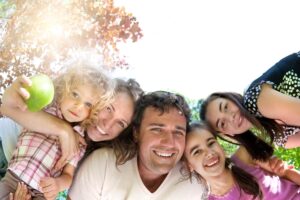A joyful group of people holding an apple, surrounded by green trees and sunlight, capturing a playful moment together.