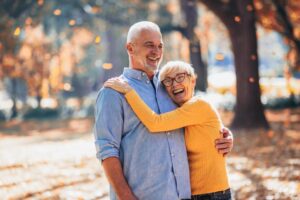 An elderly couple embraces in a sunlit autumn park, surrounded by falling leaves and warm colors.