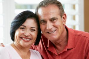 An older couple smiling closely together, with soft natural light filtering through window blinds.