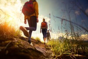 Three hikers with backpacks walking along a grassy trail during sunset, surrounded by vibrant natural scenery.
