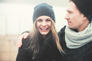 A woman in a knitted beanie and a man in a scarf embrace outdoors, surrounded by a soft, foggy atmosphere.
