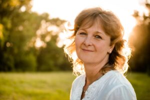 A woman in a white blouse stands outdoors, illuminated by golden sunlight, with a blurred background .