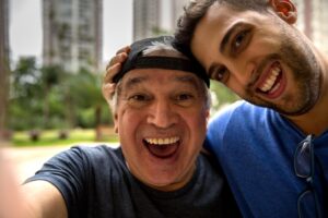 One elder and one younger man with smiley faces taking a selfie in a park.