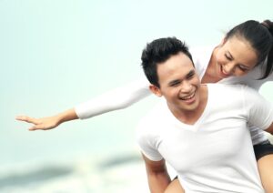 A couple enjoys a playful moment on the beach, with one person giving a piggyback ride as they smile and pose against a serene backdrop.