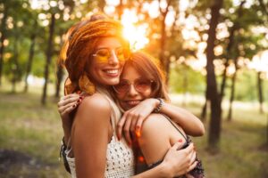 Two girl embrace in a sunlit forest, surrounded by lush greenery, radiating joy and warmth in their friendship.