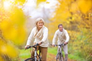 Two cyclists an woman and a man ride along a leafy path in autumn, surrounded by vibrant yellow and green foliage.