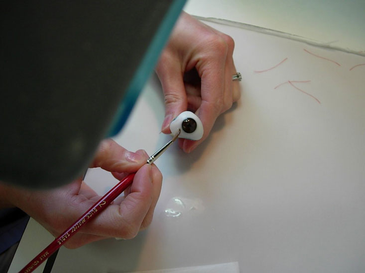 A person paints a realistic eye using a fine brush, focusing on the dark iris.