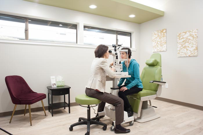 Dr. Vivian Schiedler conducts an eye examination for a lady patient with equipment.