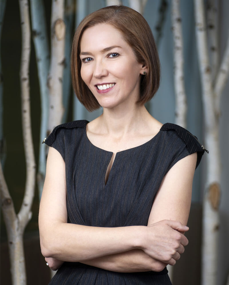 Dr. Vivian Schiedler with short hair wearing a blue dress stands confidently with a smiling face.