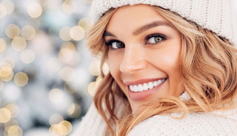 A person with long wavy hair wearing a cozy knitted sweater and hat.