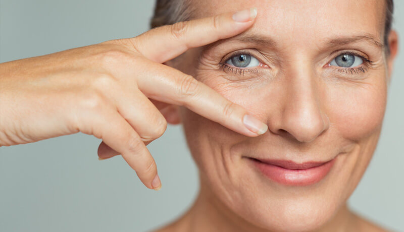 An elderly woman gesturing with fingers extended above and below of her eye.