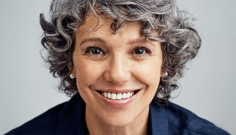 An older person with curly gray hair, wearing a navy blue shirt.