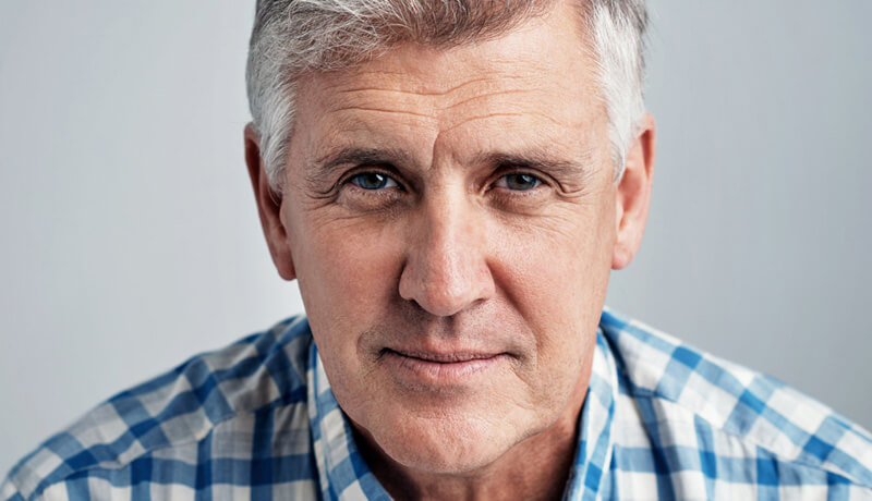 A senior man with gray hair wearing a blue and white checkered shirt.
